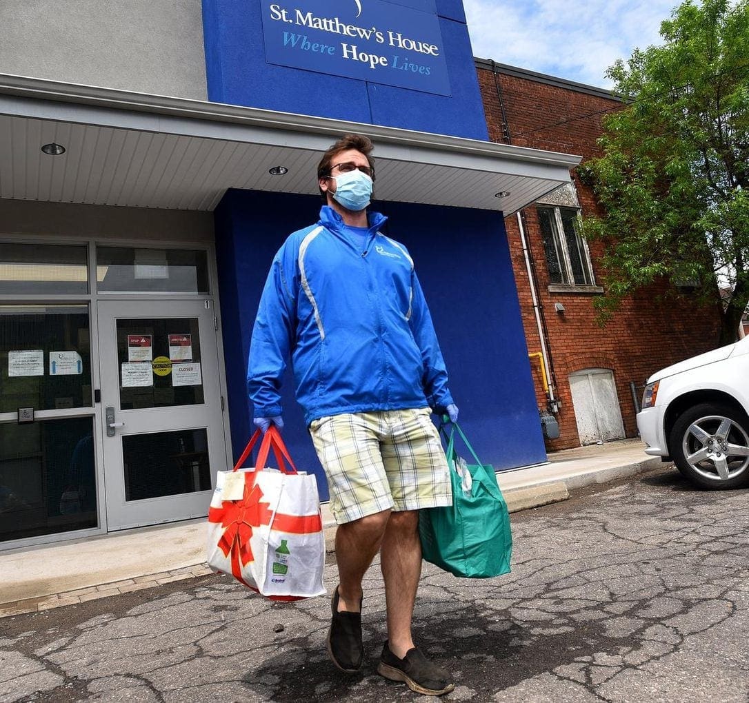 A man leaving the St. Matthew's building with groceries, wearing a mask